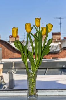 Spring bouquet of flowers in a crystal vase against the snow-covered roof. Vertical frame