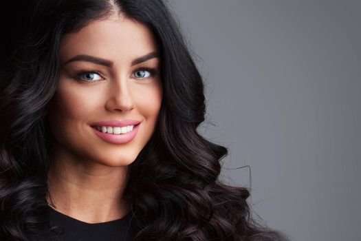 Photo of young woman with beauty long curly hair. Fashion model posing at studio over gray background