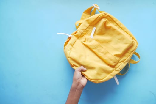 child boy hand holding a yellow backpack on blue .