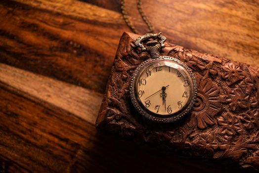 On the table are an old pocket watch over an ancient wooden case. Vintage background from a collection of antiques. Close-up and selected focus