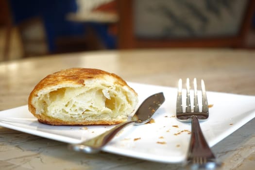 half eaten fresh baked croissant on cafe table .