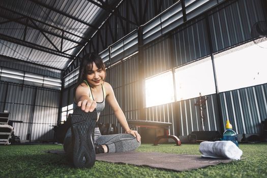 Young asian female in stylish and comfy sportswear stretching her legs on the fitness floor. exercise and sport concept. Fit woman doing stretching workout at gym.