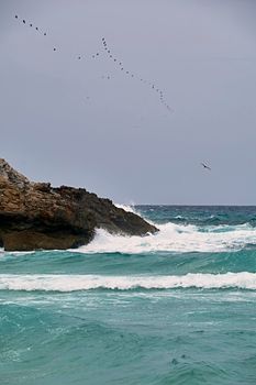 Rocks on the shore hit by the waves. Balearic Islands, Mediterranean Sea, blue sky, splashes of water.