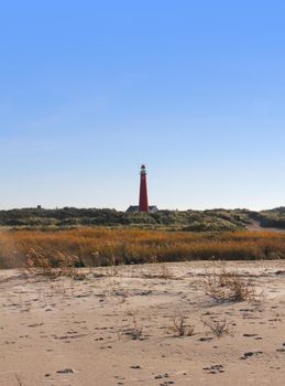 One of Schiermonnikoog's (the Netherlands) lighthouses, the Noordertoren, seen from the beach. This tower is bright red. You can see a bit of the sand and the dunes. Clear sky.