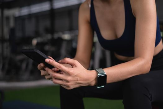 Beautiful sporty woman using phone checking her work before sports training at gym