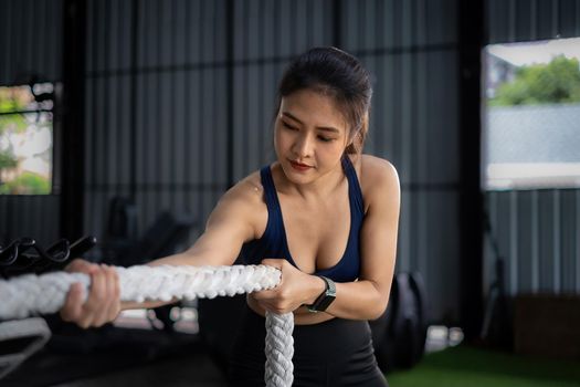 Female working out with battling rope at gym. Healthy modern people concept
