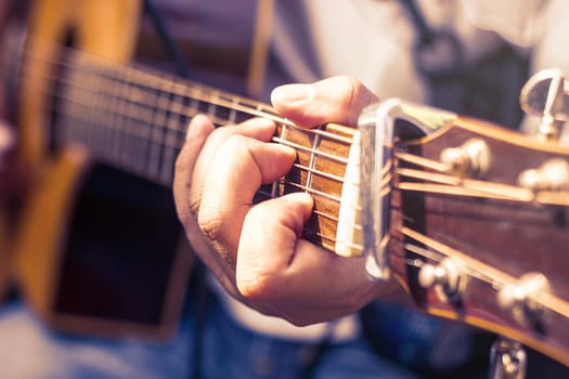 closeup of man's hands playing acoustic guitar, soft vintage style.