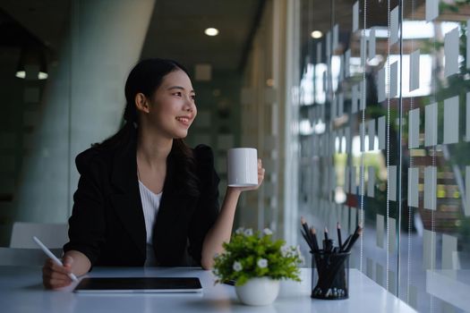 Portrait of beautiful fund managers sitting on chair with cup of cooffee and tablet on wooden desk in cafe shop