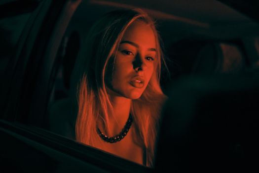 A beautiful girl of European appearance sits on the passenger seat in the car and looking to the window