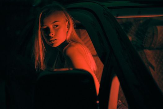 A beautiful girl of European appearance sits on the passenger seat in the car and looking to the window