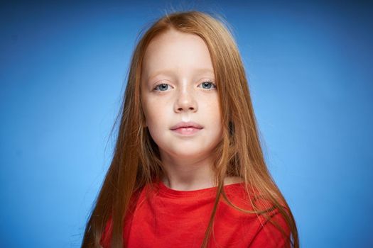 cute red-haired girl in red t-shirt emotions blue background. High quality photo