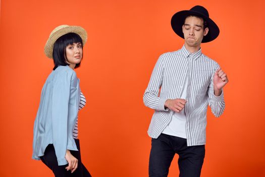 man and woman in hats posing fashion orange background. High quality photo