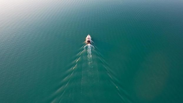 A white boat sails on Lake Balkhash at sunset. A beautiful long train on the water from the motor. The sky gradient is from orange to blue. Smooth water. Travel on a speed bot. Bertys Bay. Kazakhstan