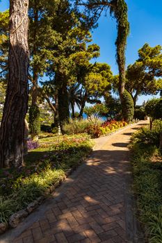 Small path in Giardini di Augusto full of colorful trees and flowers