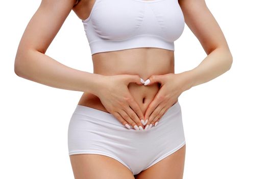 Slim woman in white underwear forming a heart symbol with her hands on her belly, isolated on white background