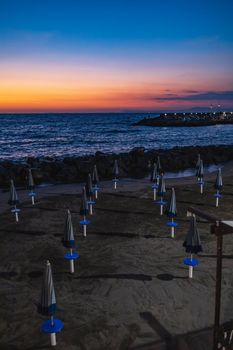 Beautiful sunset over the sea and small beach full of blue and white umbrellas next to giant rocks