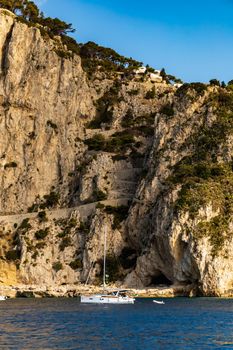 Edge of high cliff next to the sea at sunny day on Capri island with small white boat in front of