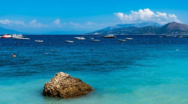 Blue azure coast next to small beach at Capri island with few boats on the sea