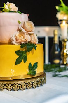 Pink and yellow wedding cake standing on table with colorful and beauty decorations around