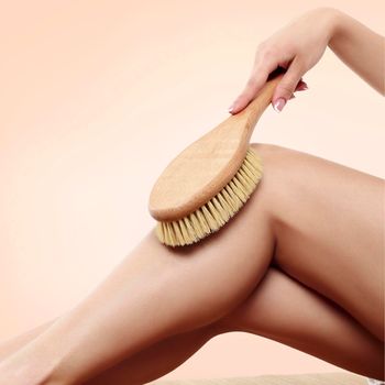 Woman is massaging skin on her legs with big brush