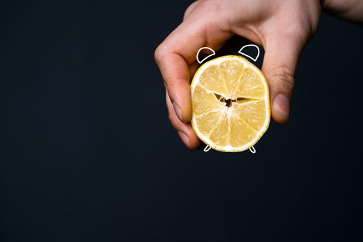 A man's hand holds a cut lemon, stylized as an alarm clock. Creative idea, fruit alarm as a symbol of regular vitamin C intake, adherence to diet and health support.