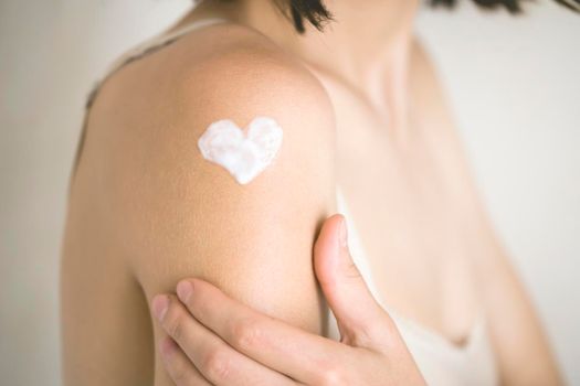 A young girl applies a moisturizer to her skin, a woman gently cares for her body, depicts a heart with a cream, taking care of herself, beauty and health.