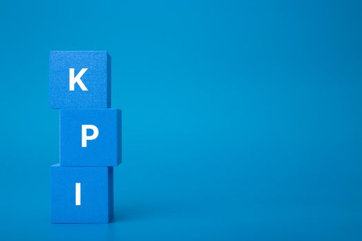 Minimal modern business KPI concept. KPI letters on stack of blue toy cubes against dark blue background with copy space. 