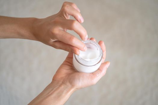 Young female hands hold a jar of moisturizing cream to maintain health, softness of the skin, the woman takes care of her health and beauty.