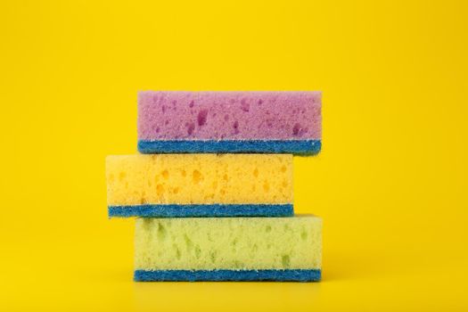 Green, purple and yellow cleaning and dishwashing sponges on yellow background. Close up, dishwashing or house cleaning concept