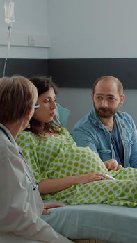 African american nurse and doctor consulting pregnant woman sitting in hospital ward. Multi ethnic medical staff talking to expecting mother and father about childbirth and assistance