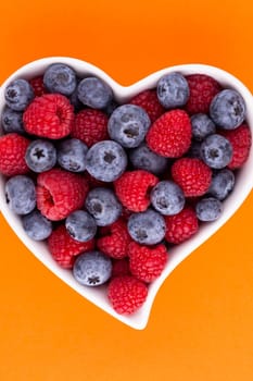 Blueberry and raspberries, fruit in a heart shaped dish on a porcelain bowl pastel background.
