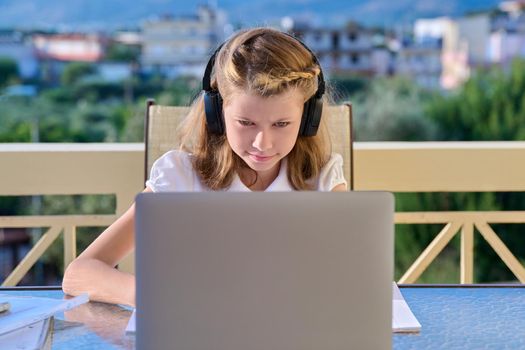 Girl child studying at home online. Pre-teen student in headphones with laptop notebooks sitting on outdoor home terrace. E-education, video chat, virtual lessons, distance learning, technology school