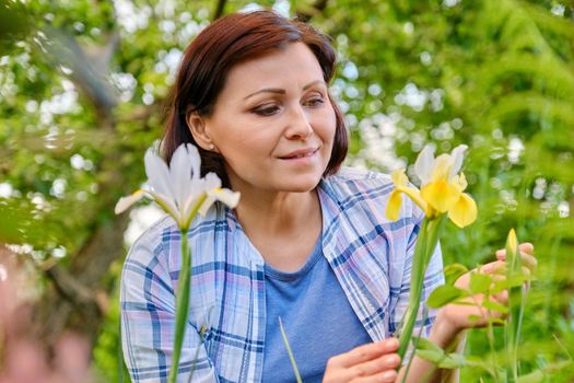 Portrait of 40s woman enjoying iris flowers in a spring garden on a flower bed. Beauty, nature, people of mature age concept