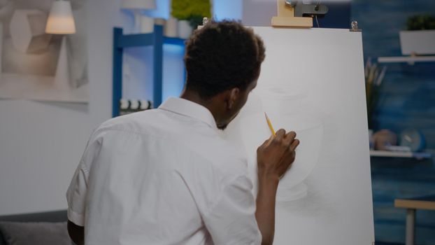 Black young artist retouching vase design on canvas and easel using pencil and art tools in creativity studio space. African american person drawing professional masterpiece for hobby