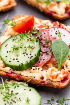 Sandwiches with cream cheese, vegetables and salami. Sandwiches with cucumber, radish, tomatoes, salami on a gray background, top view. Flat lay.