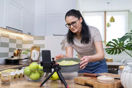 A culinary blog, a female recording a video of an apple pie recipe on a smartphone at home in the kitchen. Blogging, vlog, technology, lifestyle, hobbies and leisure, people concept