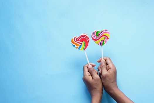 child boy hand hold rainbow heart shape candy on blue .