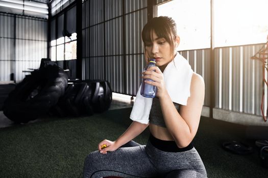 Young asian athletic woman drinking water after workout or exercise in fitness gym