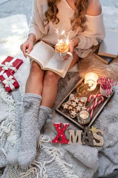 The girl is sitting in a christmas atmosphere, drinking a hot drink and reading a book.