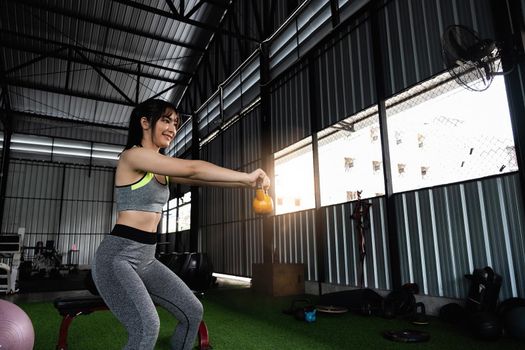 Young asian female enjoy exercising with lifting kettle bell with one hand at the gym. sport bodybuilding concept