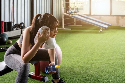 Young asian woman drinking water and wiping sweat with towel, gilr taking a break after workout in gym