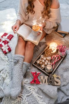 The girl is sitting in a christmas atmosphere, drinking a hot drink and reading a book.