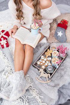 The girl is sitting in a christmas atmosphere, drinking a hot drink and reading a book.