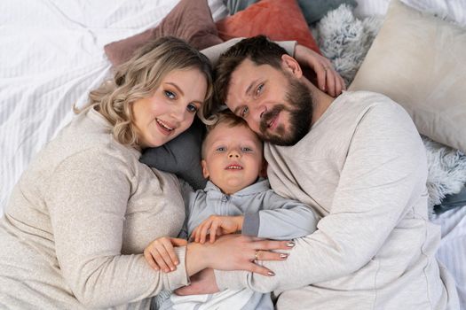 Happy family concept Mother father and little son have fun at home Caucasian family indoors Pregnant mom beard dad and funny little boy lie on the couch