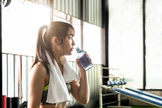 Young asian athletic woman drinking water after workout or exercise in fitness gym