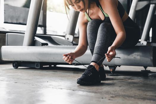 Close up of young asian woman lacing sports shoes before exercise at the gym