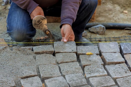 Close-up of construction worker installing and laying stones on road sidewalk with worker using stones and hammer to build stone road
