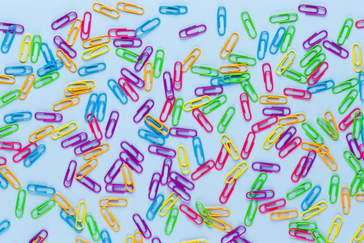Color paper clips on blue background, copy space. Top view, flat lay. Back to school, college, education concept. Collection of colorful paperclips. Abstract background.
