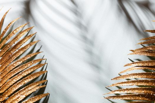 Gold palm leaves and shadows on a blue wall background.