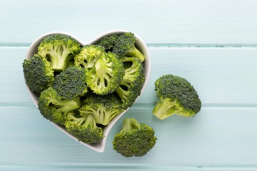 Fresh broccoli in a heart shaped bowl on a wooden background.